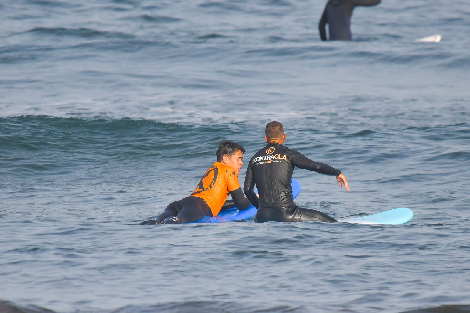 Kontraola-Surflehrer im Wasser zusammen mit einem Schüler in Playa de las Américas, Teneriffa